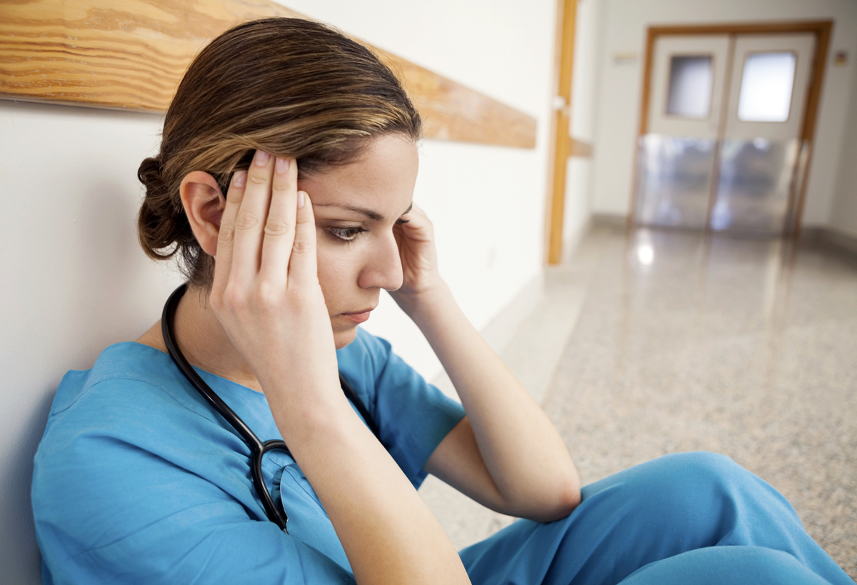 NHS nurse sitting hands on head in an empty hospital corridor